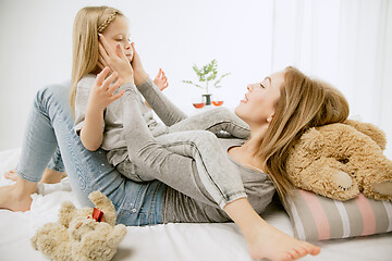 Image showing Young mother and her little daughter hugging and kissing on bed