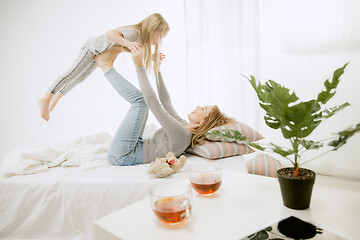 Image showing Young mother and her little daughter hugging and kissing on bed