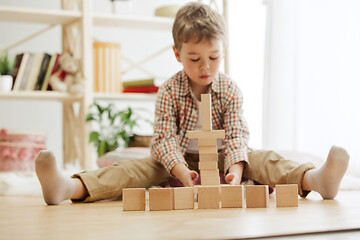 Image showing Little child sitting on the floor. Pretty boy palying with wooden cubes at home