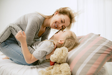 Image showing Young mother and her little daughter hugging and kissing on bed