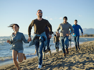 Image showing Group of friends running on beach during autumn day