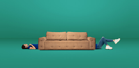 Image showing Tall high woman and long sofa isolated on green studio background. Unusual delighted and long