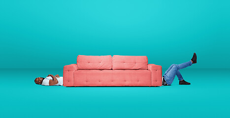 Image showing Tall high man and long sofa isolated on blue studio background. Unusual delighted and long