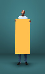 Image showing Tall high man and long yellow banner isolated on blue studio background. Unusual delighted and long