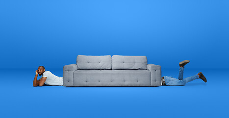 Image showing Tall high man and long sofa isolated on blue studio background. Unusual delighted and long