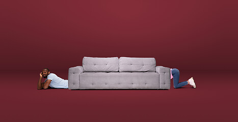 Image showing Tall high man and long sofa isolated on red studio background. Unusual delighted and long