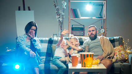 Image showing Happy family watching projector, TV, movies with popcorn in the evening at home. Mother, father and kids spending time together.