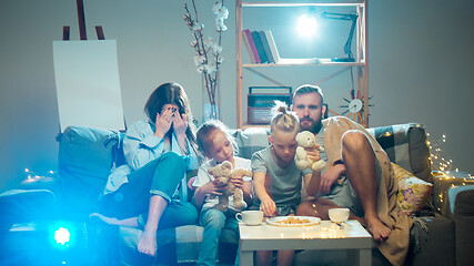 Image showing Happy family watching projector, TV, movies with popcorn in the evening at home. Mother, father and kids spending time together.