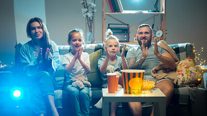 Image showing Happy family watching projector, TV, movies with popcorn in the evening at home. Mother, father and kids spending time together.