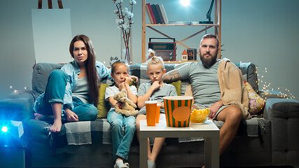 Image showing Happy family watching projector, TV, movies with popcorn in the evening at home. Mother, father and kids spending time together.