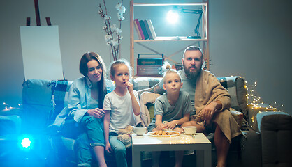 Image showing Happy family watching projector, TV, movies with popcorn in the evening at home. Mother, father and kids spending time together.