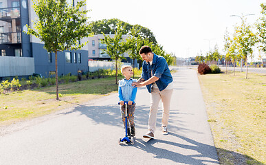 Image showing happy father and little son riding scooter in city