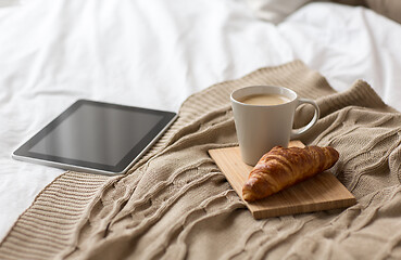 Image showing tablet pc, coffee cup and croissant on bed at home
