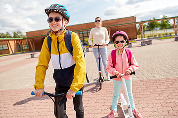 Image showing happy school children with mother riding scooters