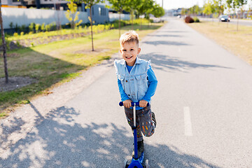 Image showing happy little boy riding scooter in city