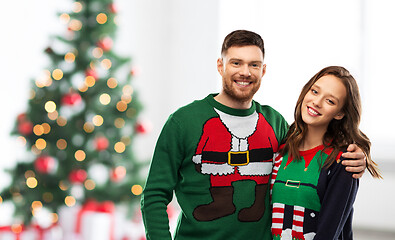 Image showing happy couple in ugly sweaters over christmas tree