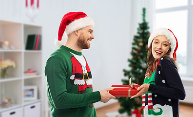 Image showing happy couple in ugly sweaters with christmas gift