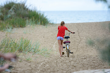 Image showing Girl drags a bicycle on the sand at the seaside