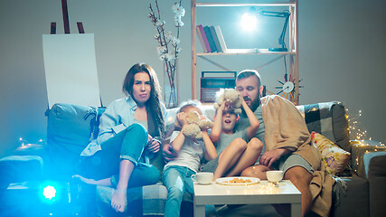 Image showing Happy family watching projector, TV, movies with popcorn in the evening at home. Mother, father and kids spending time together.