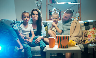 Image showing Happy family watching projector, TV, movies with popcorn in the evening at home. Mother, father and kids spending time together.