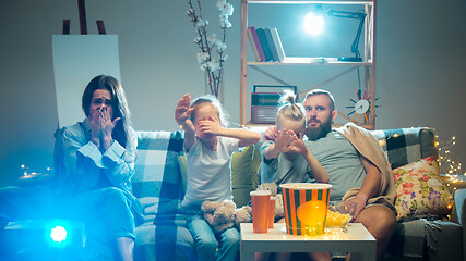 Image showing Happy family watching projector, TV, movies with popcorn in the evening at home. Mother, father and kids spending time together.