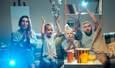 Image showing Happy family watching projector, TV, movies with popcorn in the evening at home. Mother, father and kids spending time together.