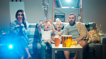 Image showing Happy family watching projector, TV, movies with popcorn in the evening at home. Mother, father and kids spending time together.