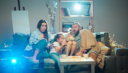 Image showing Happy family watching projector, TV, movies with popcorn in the evening at home. Mother, father and kids spending time together.