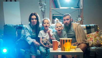 Image showing Happy family watching projector, TV, movies with popcorn in the evening at home. Mother, father and kids spending time together.