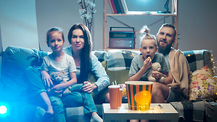 Image showing Happy family watching projector, TV, movies with popcorn in the evening at home. Mother, father and kids spending time together.