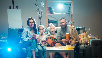 Image showing Happy family watching projector, TV, movies with popcorn in the evening at home. Mother, father and kids spending time together.