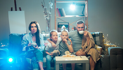 Image showing Happy family watching projector, TV, movies with popcorn in the evening at home. Mother, father and kids spending time together.