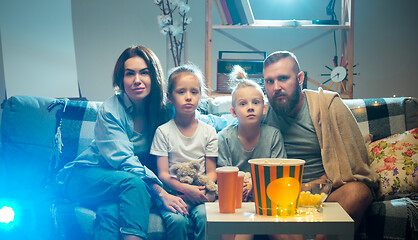 Image showing Happy family watching projector, TV, movies with popcorn in the evening at home. Mother, father and kids spending time together.