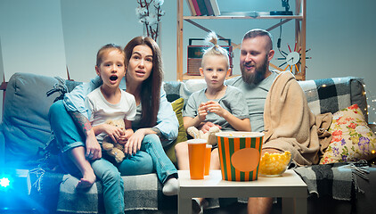 Image showing Happy family watching projector, TV, movies with popcorn in the evening at home. Mother, father and kids spending time together.