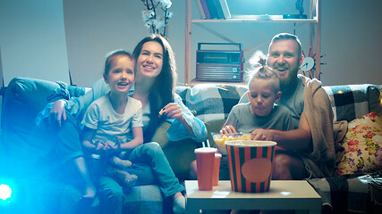 Image showing Happy family watching projector, TV, movies with popcorn in the evening at home. Mother, father and kids spending time together.