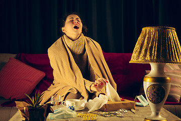 Image showing Woman wrapped in a plaid looks sick, ill, sneezing and coughing sitting at home indoors