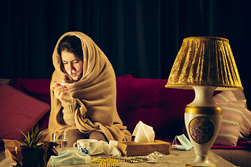 Image showing Woman wrapped in a plaid looks sick, ill, sneezing and coughing sitting at home indoors