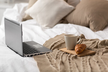 Image showing laptop, cup of coffee and croissant on bed at home