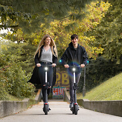 Image showing Trendy fashinable teenagers riding public rental electric scooters in urban city park. New eco-friendly modern public city transport in Ljubljana, Slovenia