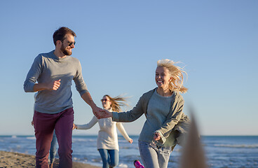 Image showing Group of friends running on beach during autumn day