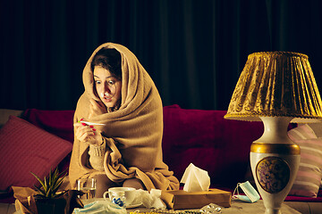 Image showing Woman wrapped in a plaid looks sick, ill, sneezing and coughing sitting at home indoors