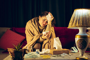 Image showing Woman wrapped in a plaid looks sick, ill, sneezing and coughing sitting at home indoors