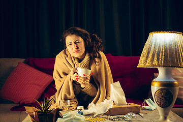 Image showing Woman wrapped in a plaid looks sick, ill, sneezing and coughing sitting at home indoors