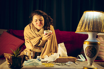 Image showing Woman wrapped in a plaid looks sick, ill, sneezing and coughing sitting at home indoors