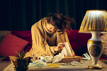 Image showing Woman wrapped in a plaid looks sick, ill, sneezing and coughing sitting at home indoors