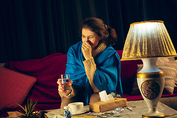 Image showing Woman wrapped in a plaid looks sick, ill, sneezing and coughing sitting at home indoors