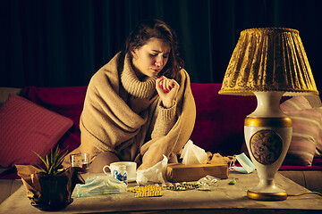 Image showing Woman wrapped in a plaid looks sick, ill, sneezing and coughing sitting at home indoors