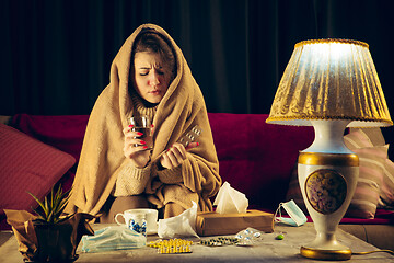 Image showing Woman wrapped in a plaid looks sick, ill, sneezing and coughing sitting at home indoors