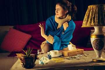 Image showing Woman wrapped in a plaid looks sick, ill, sneezing and coughing sitting at home indoors