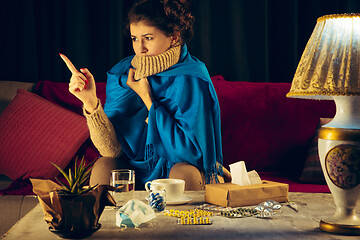 Image showing Woman wrapped in a plaid looks sick, ill, sneezing and coughing sitting at home indoors